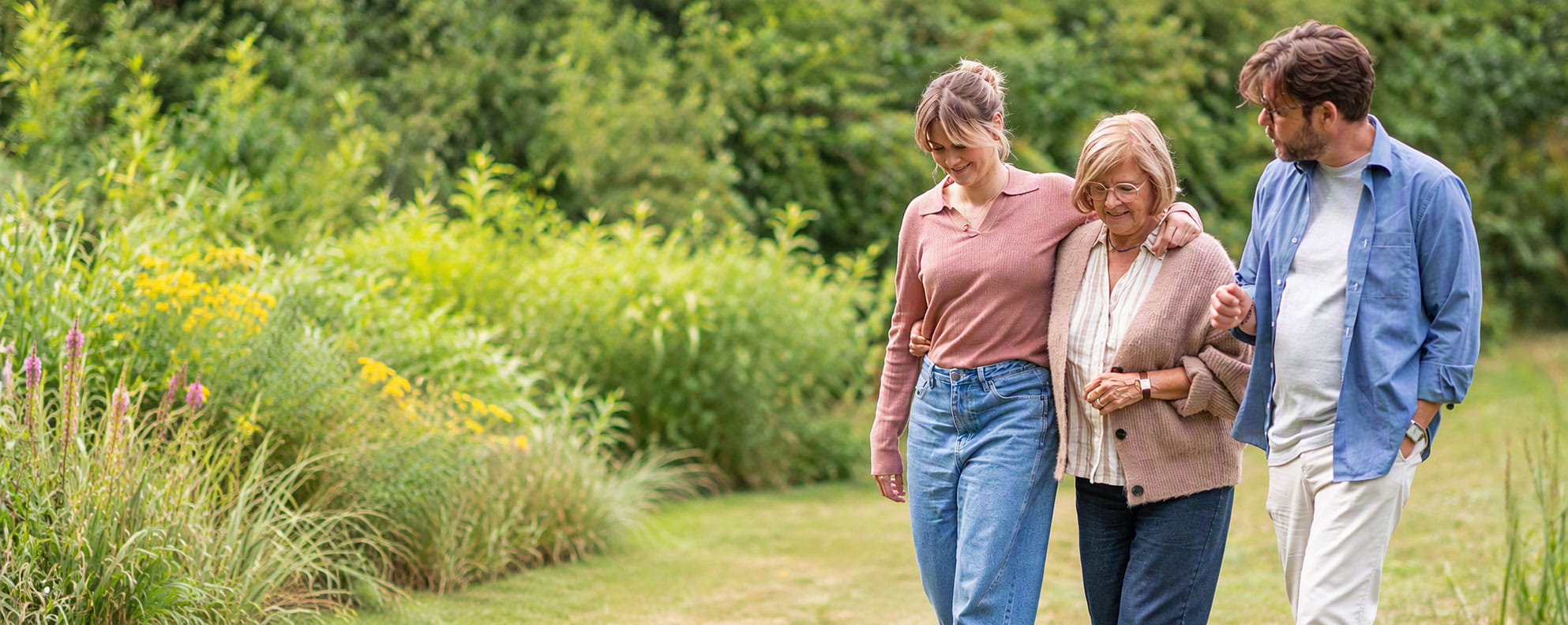 Drie personen wandelen samen op een pad in het groen.