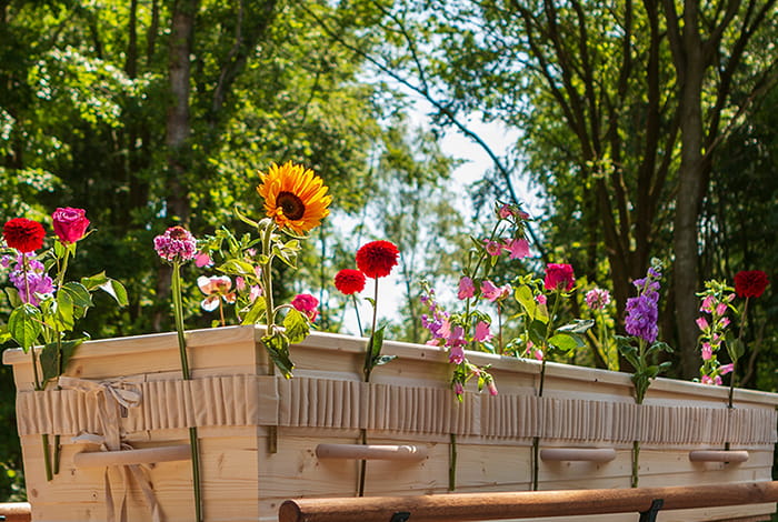 Des proches glissent des fleurs individuelles dans une bande florale entourant un cercueil lors d’une cérémonie d’hommage personnalisée. 