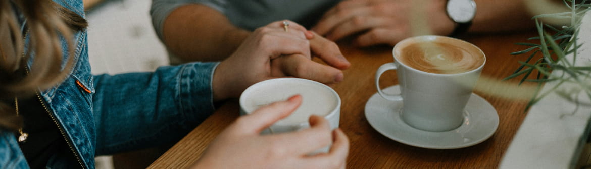 Deux personnes discutent autour d'une table en bois, un café à la main, dans l'ambiance chaleureuse d'un café.