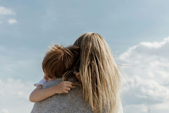 Un adulte tient un enfant dans ses bras alors qu’ils se trouvent ensemble à l’extérieur, sous un ciel dégagé.