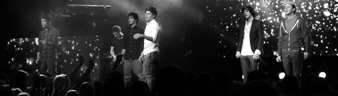 Le groupe One Direction se produit devant le public sur une grande scène de concert éclairée.