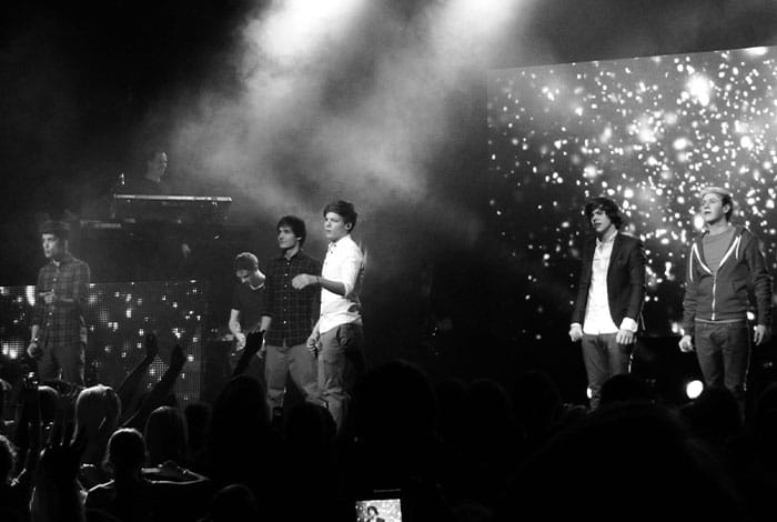 Le groupe One Direction se produit devant le public sur une grande scène de concert éclairée.