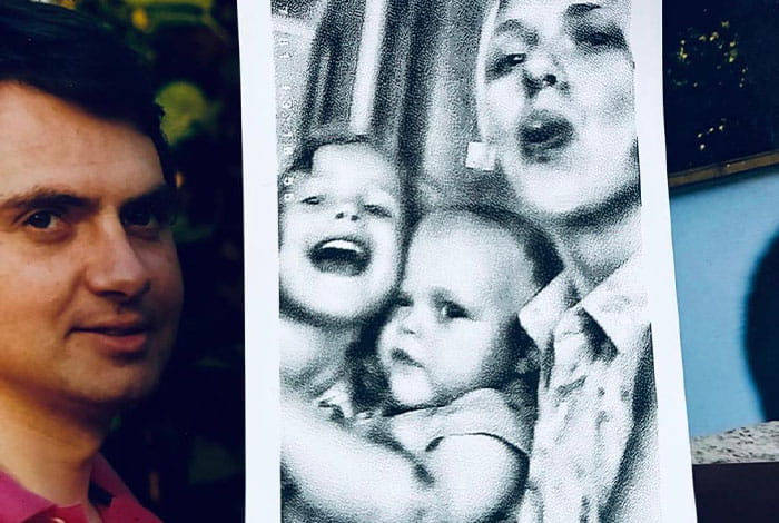 Gros plan de plusieurs photos de famille imprimées. Au centre, une photo en noir et blanc montre un adulte tenant deux jeunes enfants dans les bras. À gauche, un portrait séparé est visible. Les photos sont disposées côte à côte et évoquent les souvenirs et les liens affectifs.