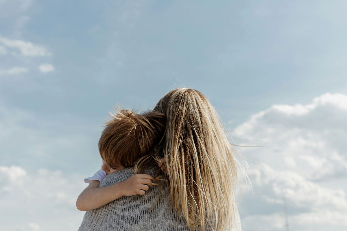 Adulte tenant un enfant dans ses bras à l'extérieur, sous un ciel dégagé.