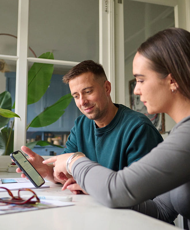Twee personen bespreken informatie op een smartphone tijdens een gesprek aan tafel.
