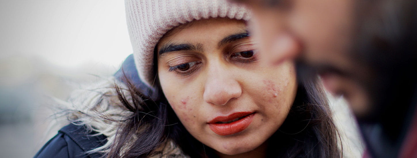 Close-up van twee personen dicht bij elkaar buiten, één persoon scherp in beeld met muts en winterjas, de andere persoon op de voorgrond onscherp